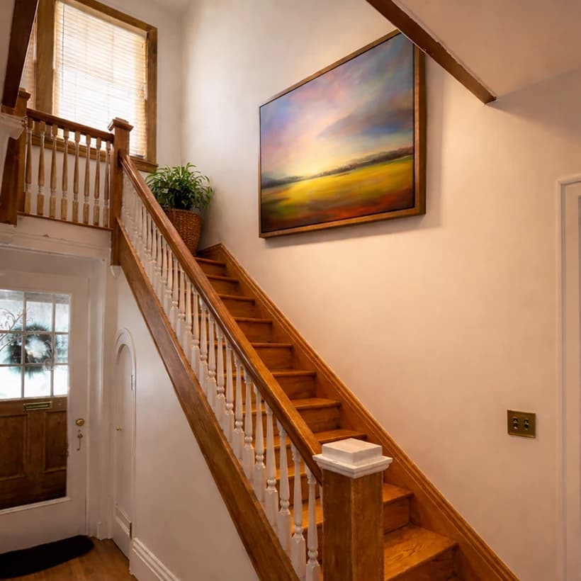 Vibrant sunset landscape painting hung along a stairway with exposed wooden beams